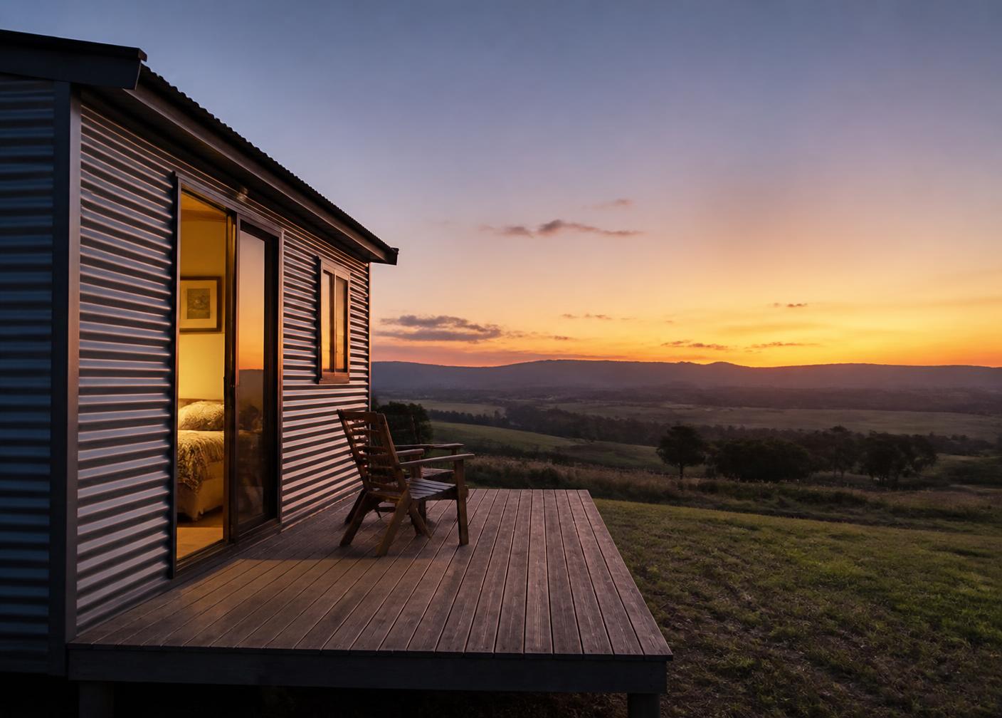 Self-contained cabin with a timber deck looking over farmland at dusk